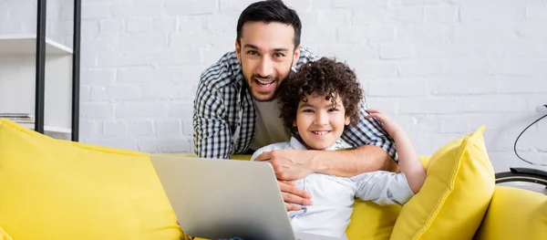 Feliz Hombre Musulmán Abrazando Sonriente Hijo Sentado Sofá Con Ordenador —  Fotos de Stock