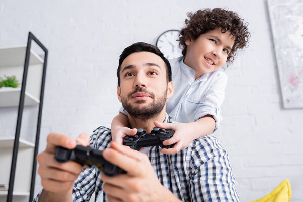 КИЕВ, УКРАИНА - 15 ЯНВАРЯ 2021: возбужденный мальчик-мусульманин, играющий с улыбающимся отцом, размытый передний план