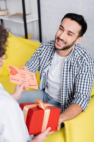 pleased arabian man taking present and i love you dad card from son on blurred foreground