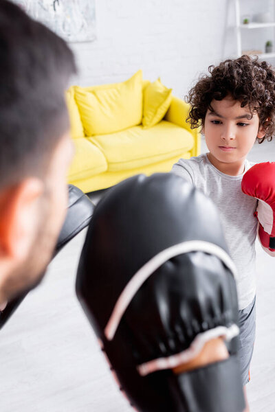 Muslim boy boxing during training with father in punch mitts on blurred foreground 