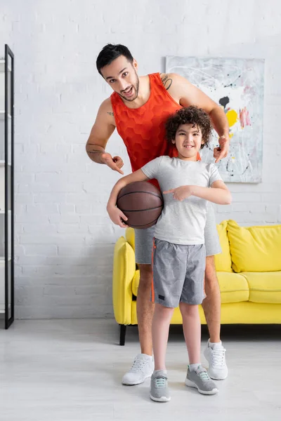 Cheerful muslim son and father pointing at basketball at home