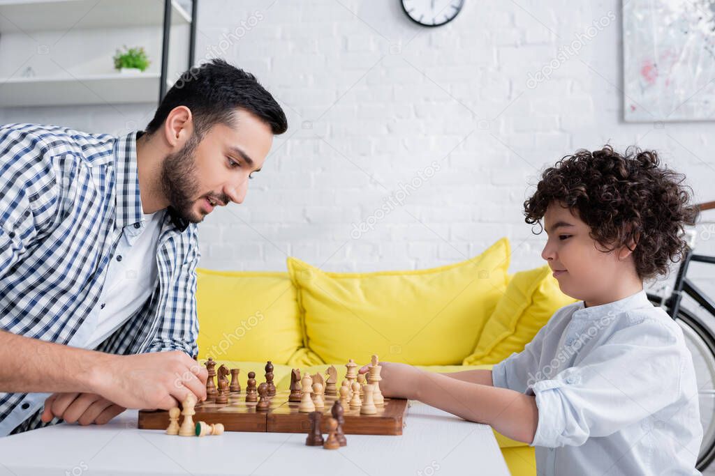side view of arabian father and son playing chess at home