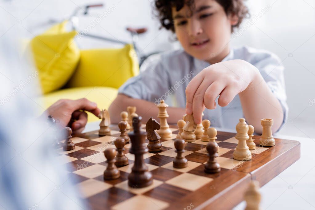 selective focus of chessboard near muslim boy and father playing at home