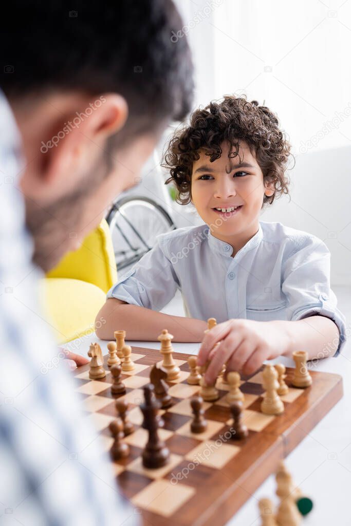 smiling arabian boy playing chess with dad on blurred foreground