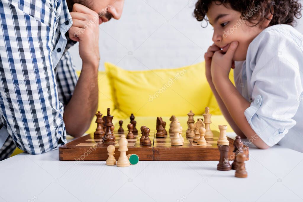 Chess on board near pensive arabian boy playing with father on blurred background 