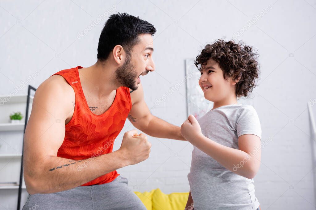 Cheerful muslim man in sportswear looking at son at home 