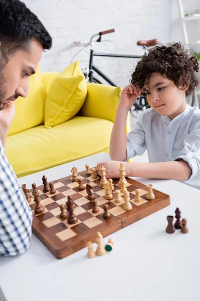 Arap çocuk, babasının yanındaki satranca bakıyor oturma odasında bulanık bir ön planda. 