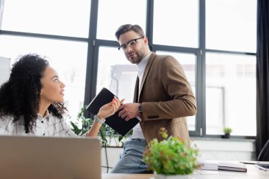 Afro-Amerikan meslektaşının yanındaki dizüstü bilgisayara bakan bir iş adamı. 