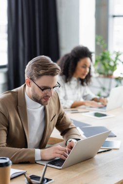 Ofis masasındaki aletlerin yanında dizüstü bilgisayar kullanan bir işadamı. 