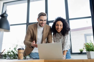 Fabrika ve kahvenin yanında dizüstü bilgisayar kullanan çok ırklı iş adamları ön planda bulanıklık yaratıyor 