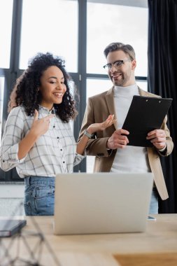 Bulanık ön planda pano ve dizüstü bilgisayarla çalışan pozitif ırklar arası iş adamları 