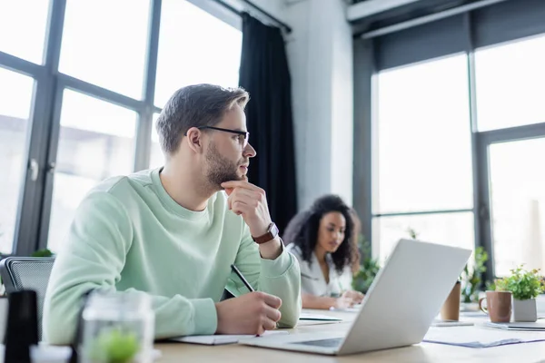 Geschäftsmann Schreibt Auf Notizbuch Neben Laptop Auf Verschwommenem Vordergrund — Stockfoto