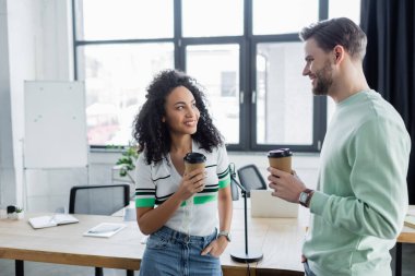 Ofiste konuşurken kahve içen neşeli çok kültürlü yöneticiler.