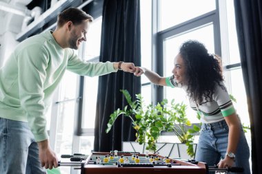 Neşeli ırklar arası iş ortakları masa futbolu oynarken yumruk tokuşturuyorlar.