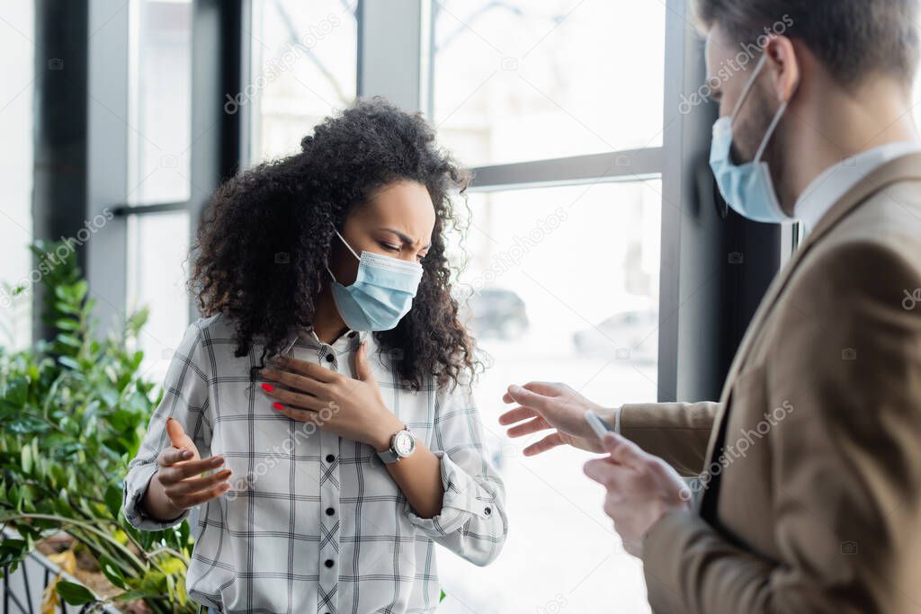 businessman standing with outstretched hand near coughing african american colleague