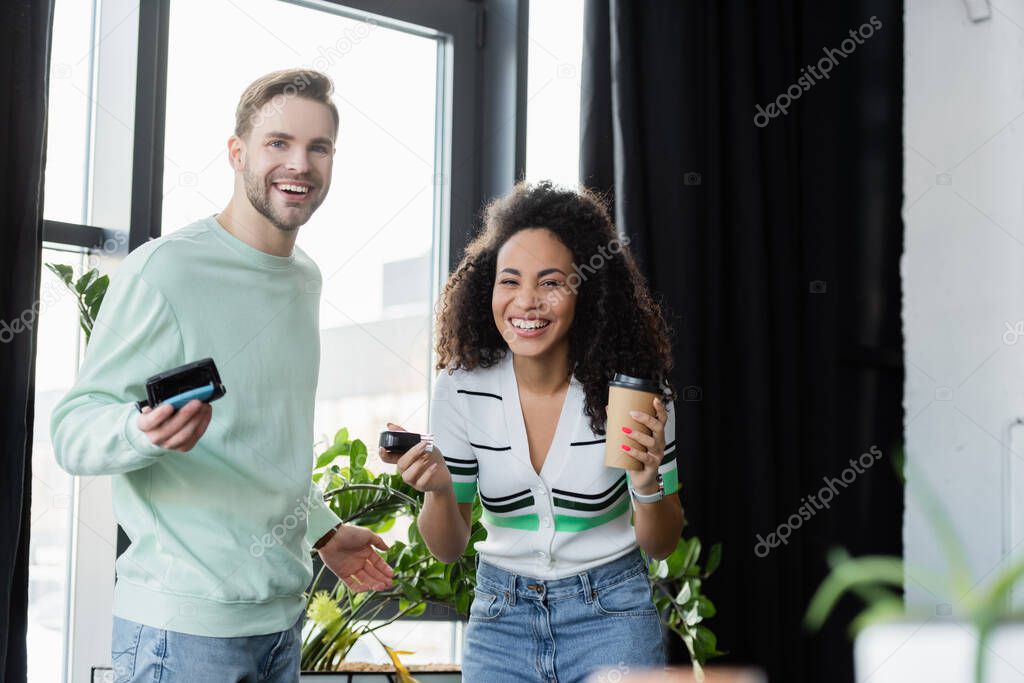 happy interracial business colleagues looking at camera while holding automatic stamps