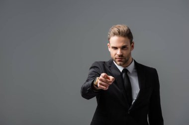 strict businessman pointing with finger while looking at camera isolated on grey clipart