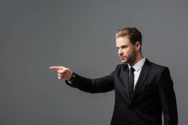 serious businessman looking away and pointing with finger isolated on grey clipart