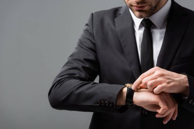 cropped view of businessman checking time on wristwatch isolated on grey clipart