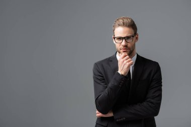 Düşünceli iş adamı, gri kameraya bakarken çenesine dokunuyor.