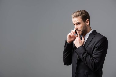Düşünceli iş adamı, gri telefonda konuşurken dudaklarına dokunuyor.