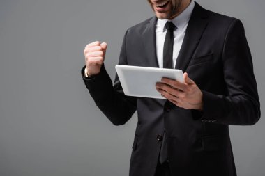partial view of successful businessman with digital tablet showing win gesture isolated on grey clipart