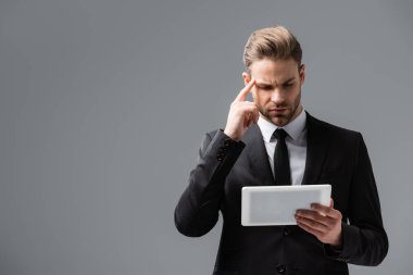 Düşünceli işadamı gri tablete bakarken kafaya dokunuyor.