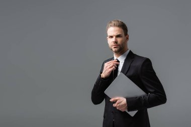 Ciddi iş adamı dizüstü bilgisayarını tutarken kravatını gri renkte ayarlıyor