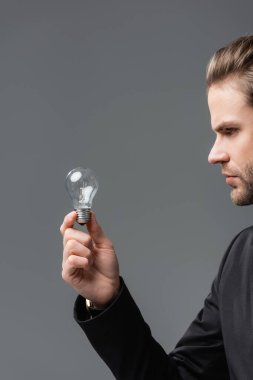 young businessman holding light bulb isolated on grey clipart