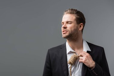 Stresli iş adamı gözleri kapalı, boynuna halatla dokunuyor. Gri üzerinde izole edilmiş.