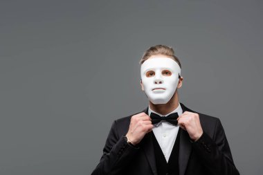 elegant businessman in face mask adjusting bow tie isolated on grey clipart