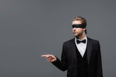 Gözleri bağlı siyah takım elbiseli iş adamı, gri üzerine parmak işareti yapıyor.