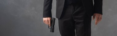 partial view of businessman in black suit holding weapon on grey background with smoke, banner clipart