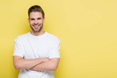 happy man smiling at camera while standing with crossed arms on yellow clipart