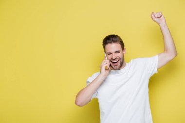 Heyecanlı adam, sarı telefonda konuşurken neşeli bir hareket sergiliyor.