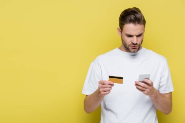 Ciddi bir adam elinde sarı kart tutarken akıllı telefonuyla daktilo çekiyor.
