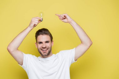 inspired man pointing at light bulb while looking at camera on yellow clipart