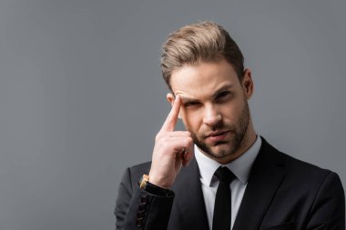 Genç, düşünceli iş adamı, gri kafaya dokunurken kameraya bakıyor.