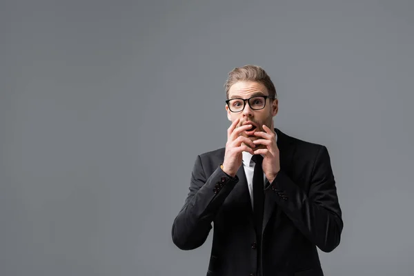 afraid businessman covering mouth with hands while looking at camera isolated on grey