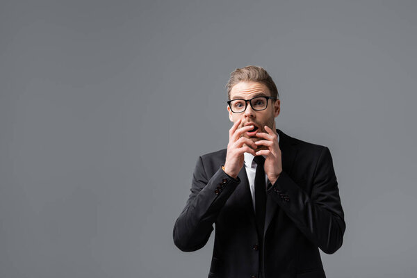 боящийся, что бизнесмен закрывает рот руками, глядя на камеру, изолированную на сером