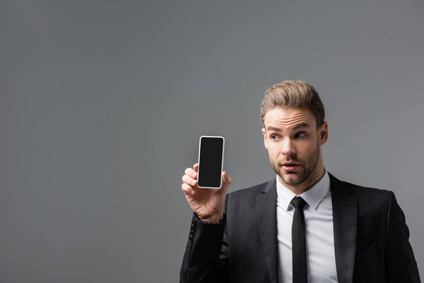 curious businessman holding mobile phone with blank screen isolated on grey
