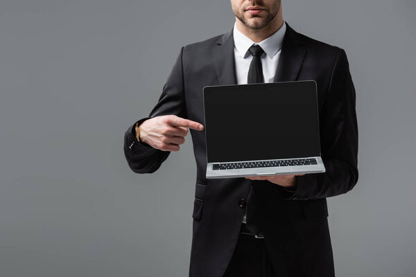 cropped view of manager in formal wear pointing at laptop with blank screen isolated on grey