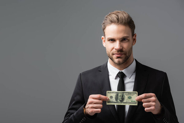 serious manager holding dollar banknote while looking at camera isolated on grey