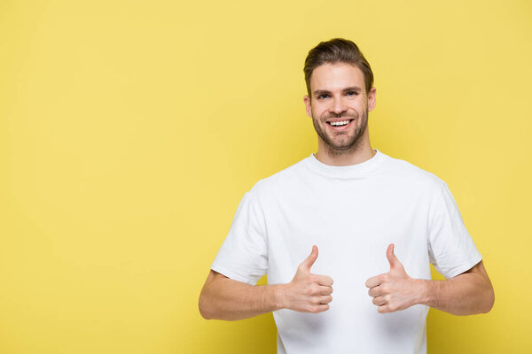 pleased man smiling at camera and showing thumbs up on yellow
