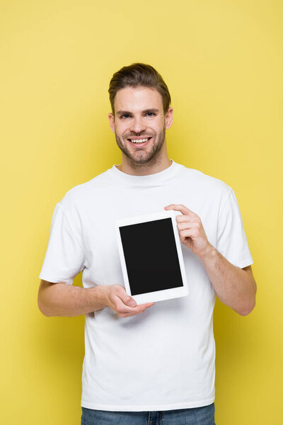 joyful man holding digital tablet with blank screen while looking at camera on yellow