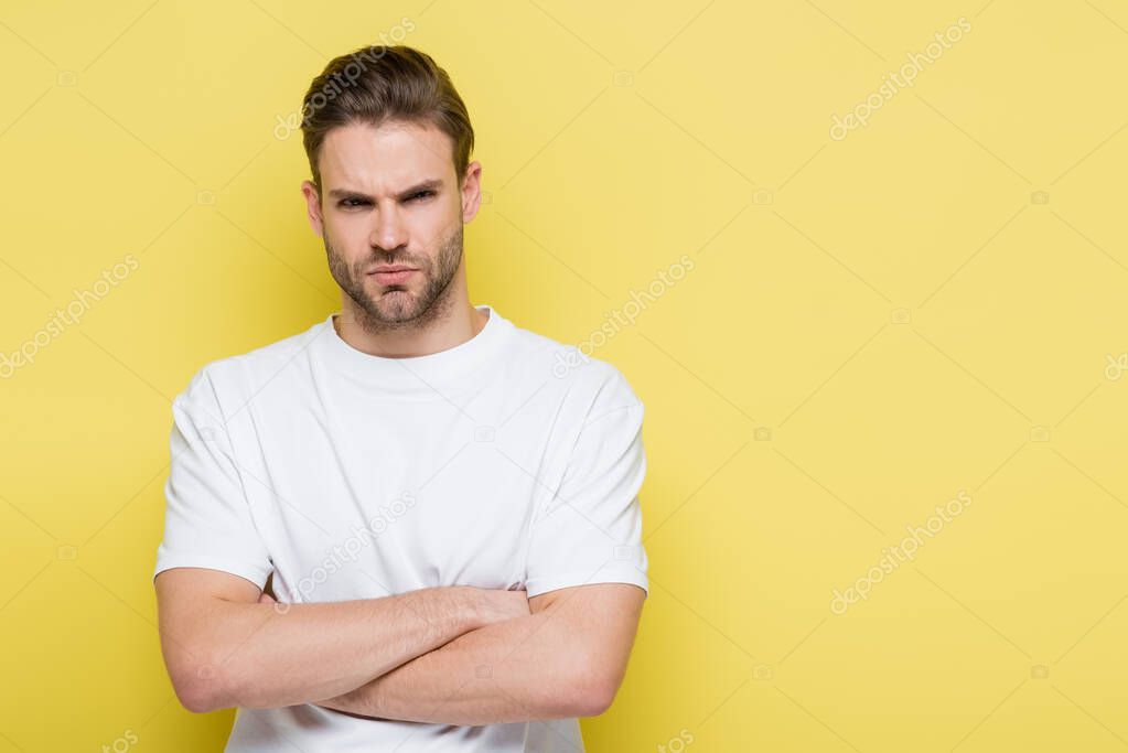 angry man looking at camera while standing with crossed arms on yellow