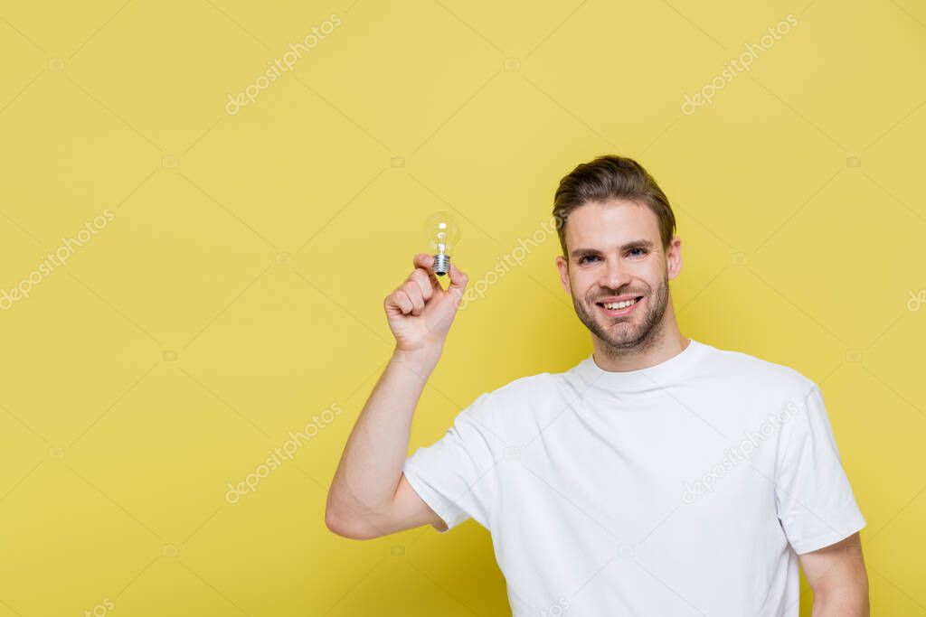 joyful man holding light bulb while smiling at camera on yellow