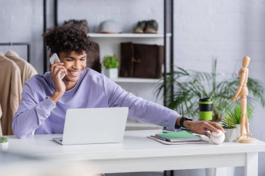 Gülümseyen Afrikalı Amerikalı galeri sahibi akıllı telefondan konuşuyor ve beyzbol topu tutuyor. 