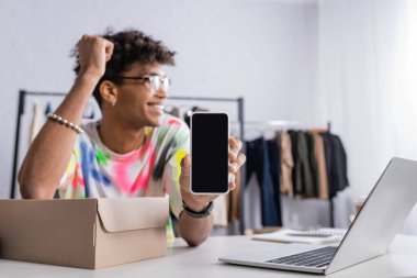 Akıllı telefon, dizüstü bilgisayarın ve kutunun yanındaki Afrikalı Amerikalı küçük işletme sahibinin elinde. 