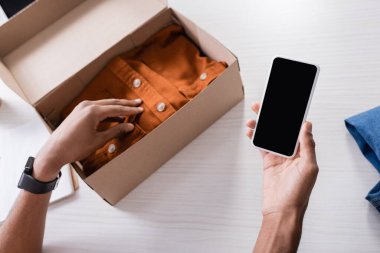 Afro-Amerikan iş adamının elinde akıllı telefon varken kıyafetleri bulanık arka planda kutuya koyduğu görüntüler. 